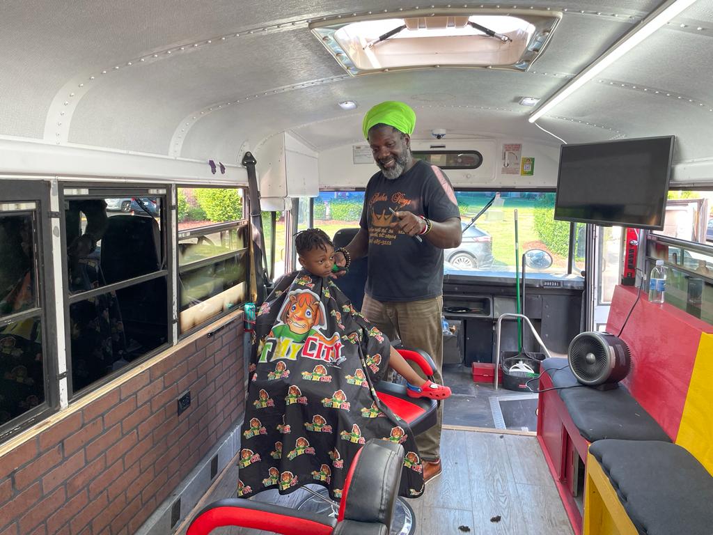 A male child sitting in a chair with an older male standing next to him cutting his hair