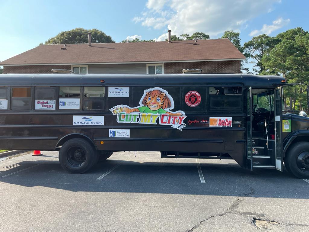 A black school bus with the logo of a tiger with the words Cut My City under the tiger. This bus is used to give hair cuts